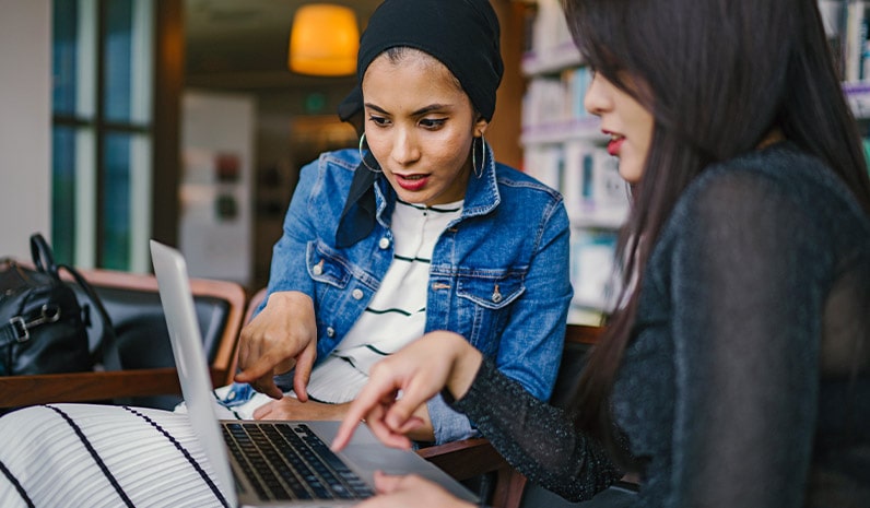 two women pointing at laptop they are working on