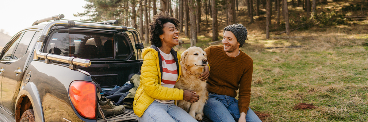 man and woman sitting on a tailgate, petting a golden lab dog in between them