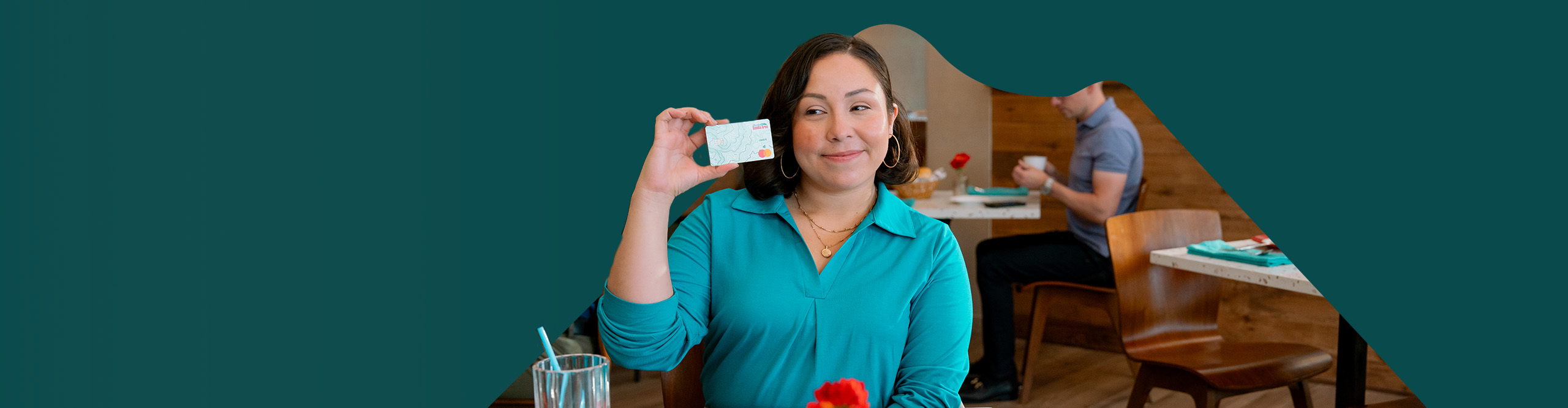 woman in teal shirt sits at a restaurant holding a Sandia Area debit card