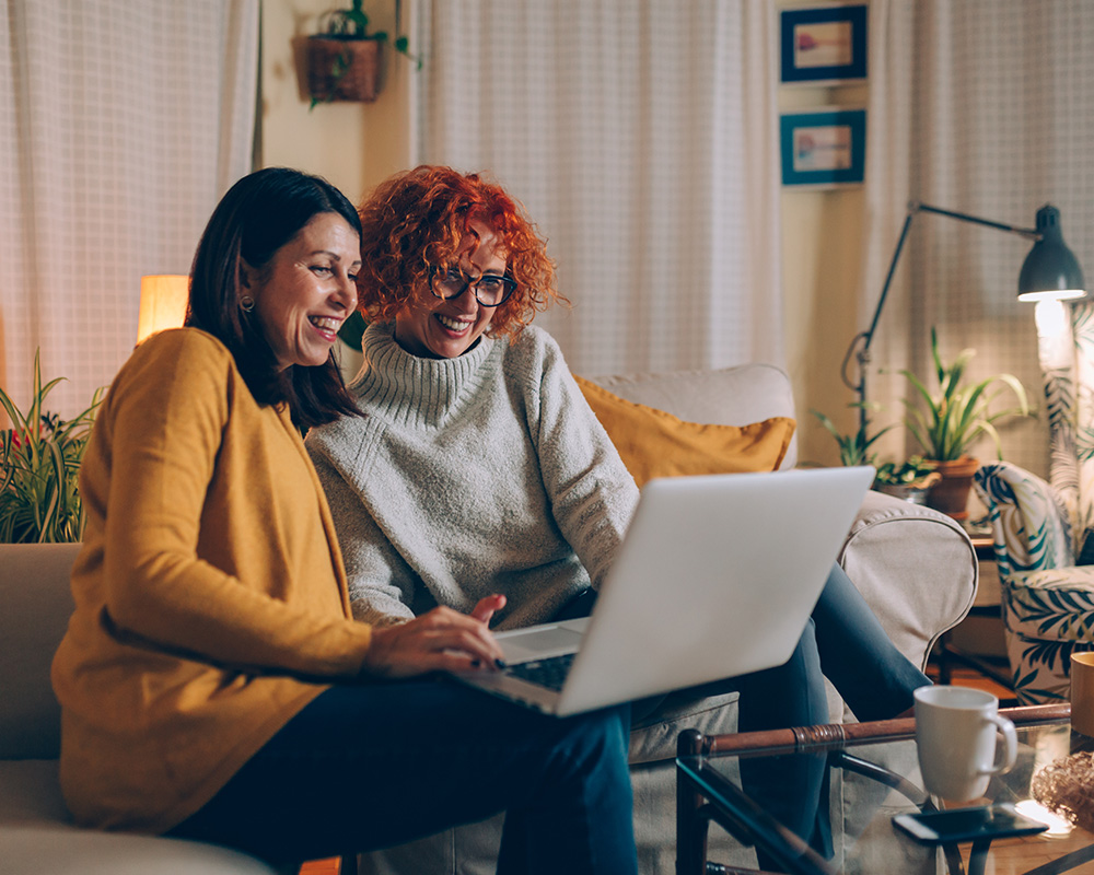 two women sitting on couch looking at computer