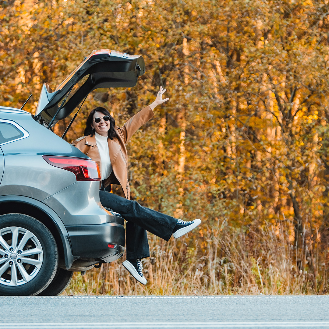 woman in trunk of car next to leaves with orange trees