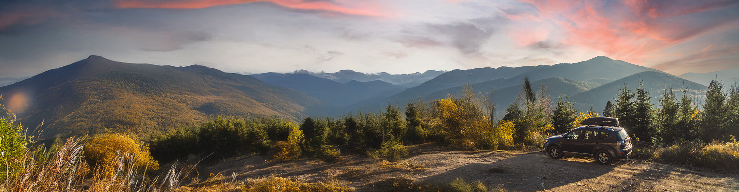 black car parked at an overview spot in the mountains with sunset