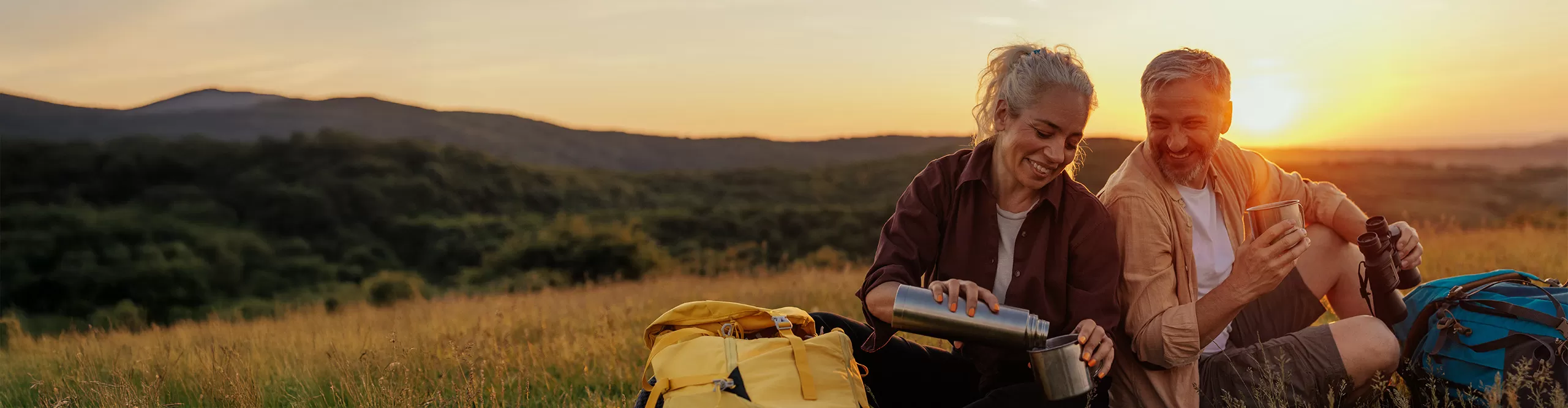 man and woman pouring a drink from a thermos at sunset